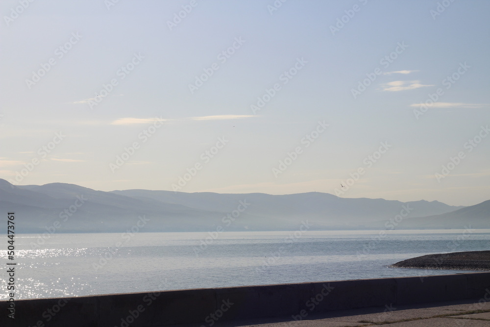 Morning sea and mountains. Calm light sea with reflections on the water.