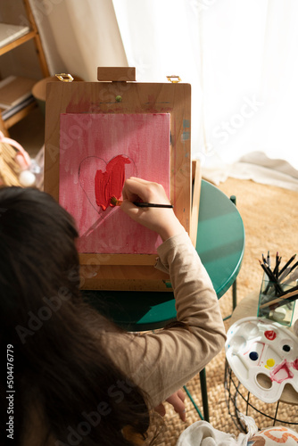 Girl painting red heart to give to mom at home photo