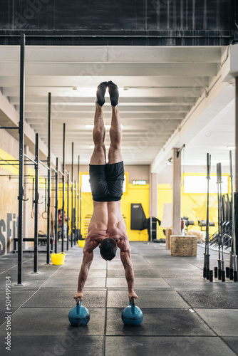 Sportsman performing handstand on kettlebells in gym