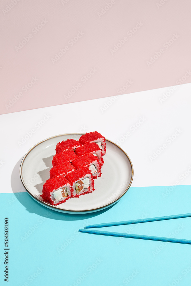 Fototapeta premium California maki roll with tobiko caviar on modern coloured background. Sushi roll with salmon and cucumber inside, tobiko caviar outside. Colourful maki sushi in minimal style. Japanese menu concept.