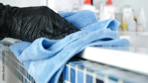Cleaning service concept. Housemaid from hotel or beauty clinic staff in uniform and black protective gloves cleaning tile and sink with wipe using liquid detergent cleaner. disinfecting surfaces from