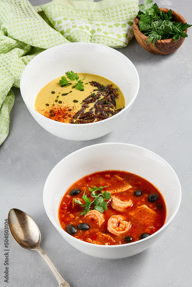 Composition with cream soup and tomato seafood soup. Set of soups on concrete background. Aesthetic composition with vegetables soup and fish soup in white ceramic bowl Composition with cream soup and tomato seafood soup. Set of soups on concrete background. Aesthetic composition with vegetables soup and fish soup in white ceramic bowl