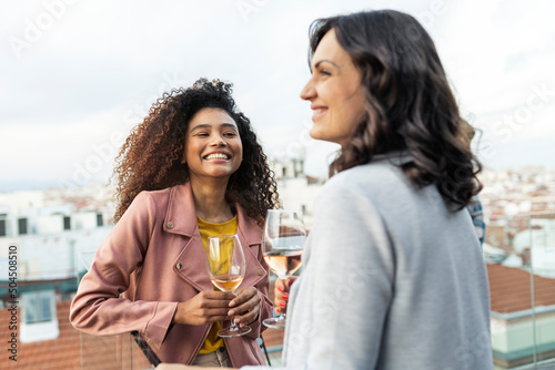 Smiling diverse women with white wine on rooftop