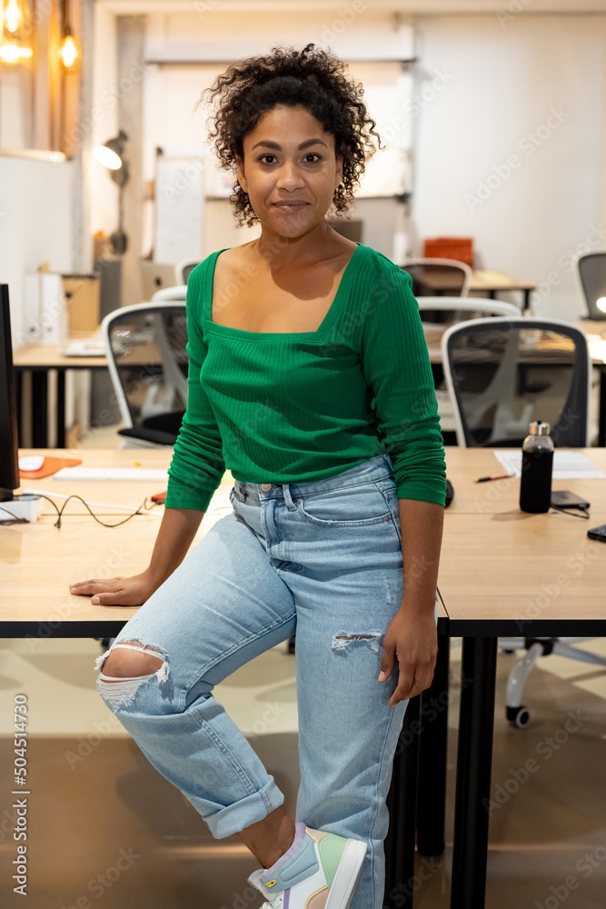 Black female employee sitting on table in office Black female employee sitting on table in office