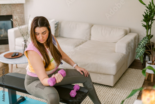 Curvy woman toning arms with dumbbells at home
