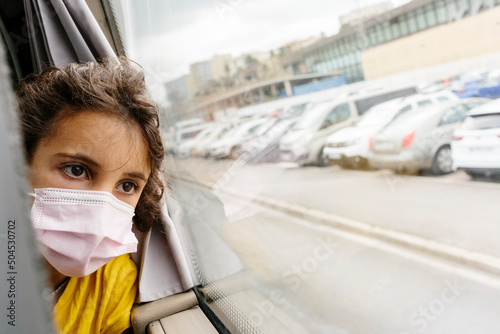 Kid with face-mask leaning in window of bus oon the road photo