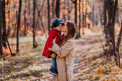 Mother kissing her daughter in a red coat in autumn forest © Stas Vedutenko