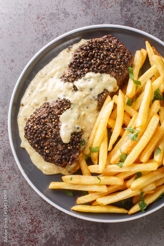 Homemade Steak Au Poivre with Pepper Sauce served with french fries close-up in a plate on the table. Verttical top view from above photo