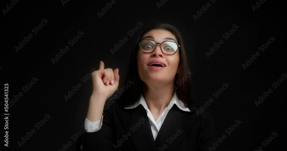 Thoughtful business smart woman in a black jacket is considering a solution to the problem. Asian woman with long dark hair came up with an idea, and she shows her index finger up. Black background Thoughtful business smart woman in a black jacket is considering a solution to the problem. Asian woman with long dark hair came up with an idea, and she shows her index finger up. Black background