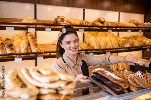 Pretty woman in apron selling freshly baked pastry and bread in bakery shop.