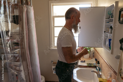 Man in bathroom looking in medicine cabinet.