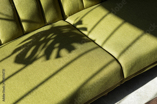 A beautiful light on a green couch with a monstera shadow on it photo