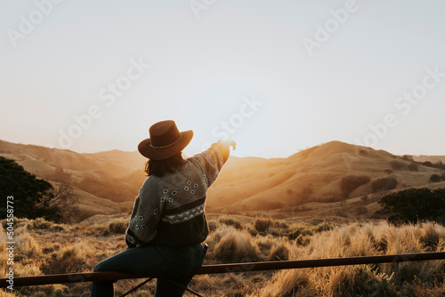 Seated woman pointing at the sunset