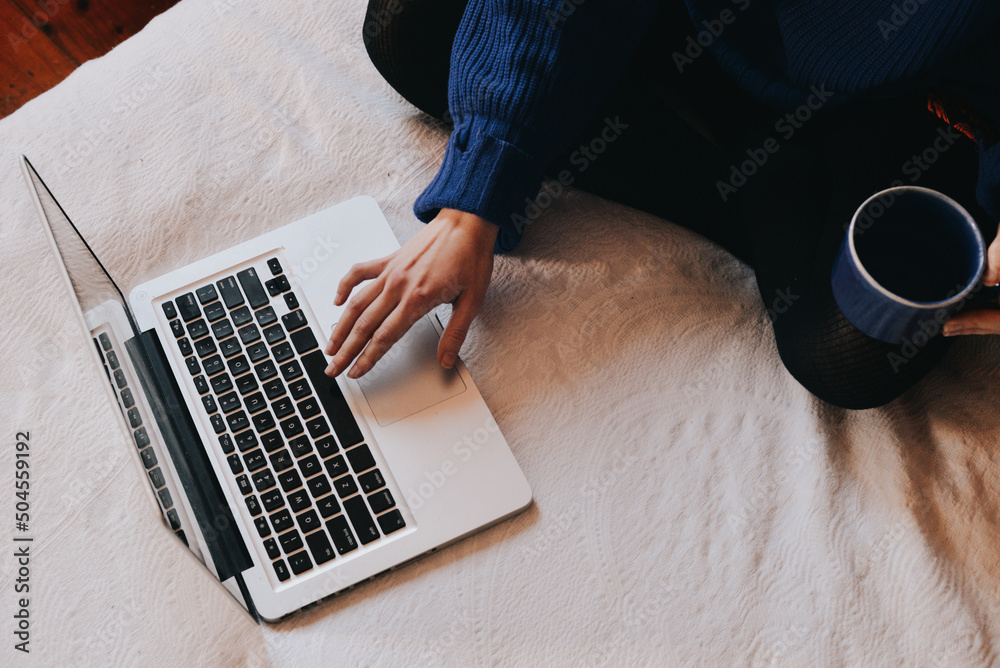 © Anna Malgina/Stocksy - A woman working in bed with her laptop