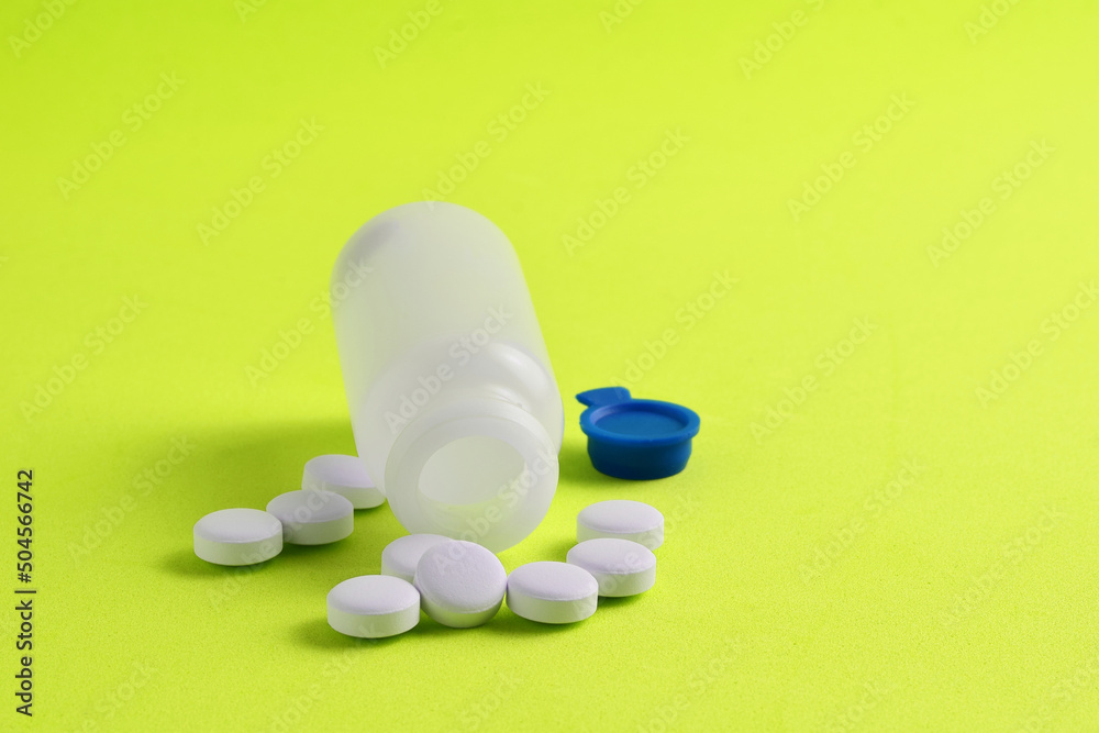 Medication, rounded white tablets and small bottle on a green background. Medication, rounded white tablets and small bottle on a green background.