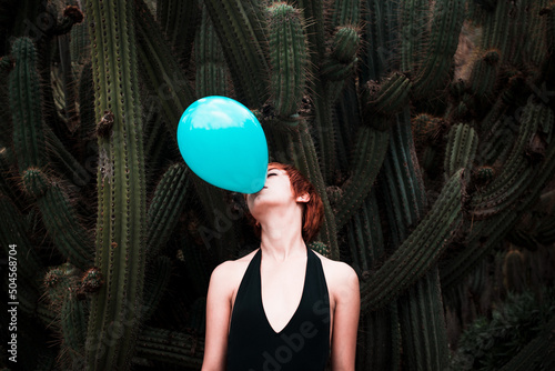 Woman blowing up blue balloon with cactus background photo
