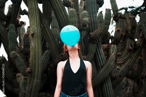 Conceptual portrait of woman blowing ballon with cactus background  photo