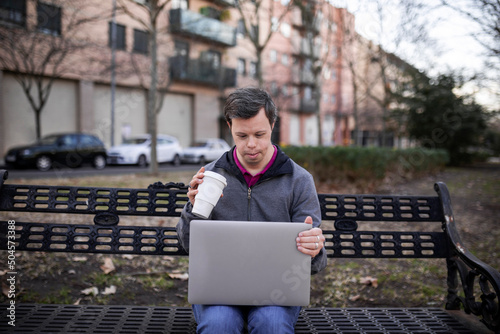 Young man with down syndrome with a laptop in a park photo