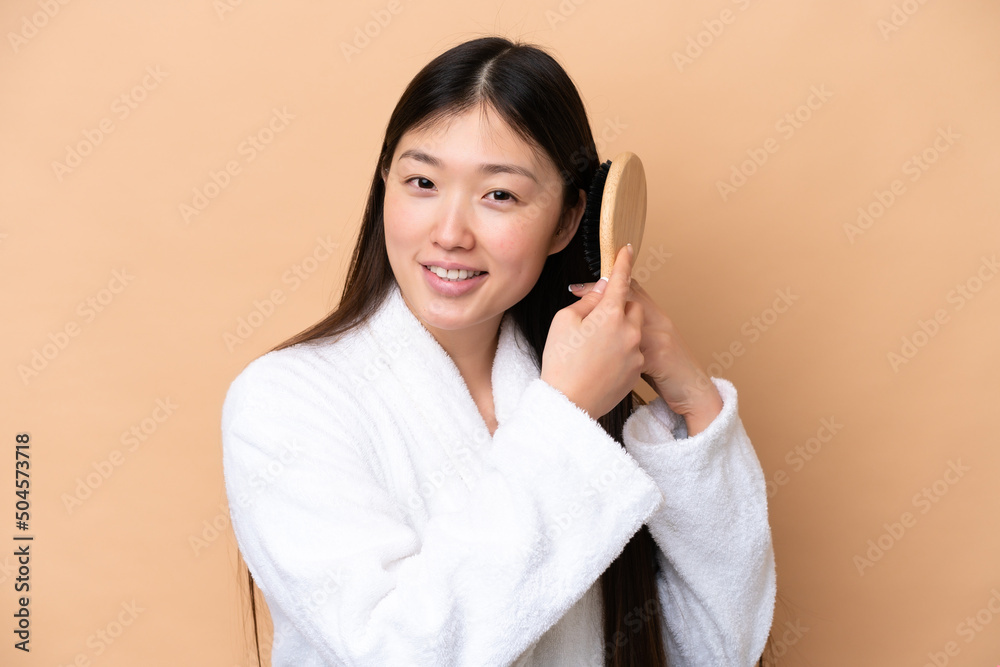 Young Chinese woman isolated on beige background with hair comb Young Chinese woman isolated on beige background with hair comb