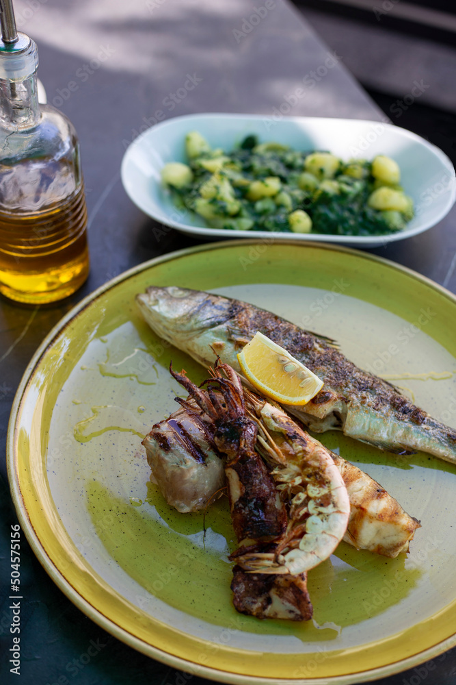 Grilled seafood mix - squid, shrimp, trout with lemon and potato salad with spinach. Croatian cuisine