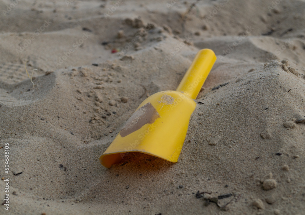 Yellow plastic shovel in and beach sand. Yellow plastic spatula. Fun in the sand Yellow plastic shovel in and beach sand. Yellow plastic spatula. Fun in the sand