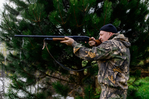 Hunter aims a gun against the backdrop of a misty lake and picea