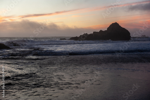 Tidal waves flowing out at Pfeiffer beach, while it is enshrouded by a purble sunset color.