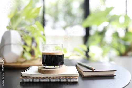 Espresso coffee in a glass cup and notebook and plant pot on black table