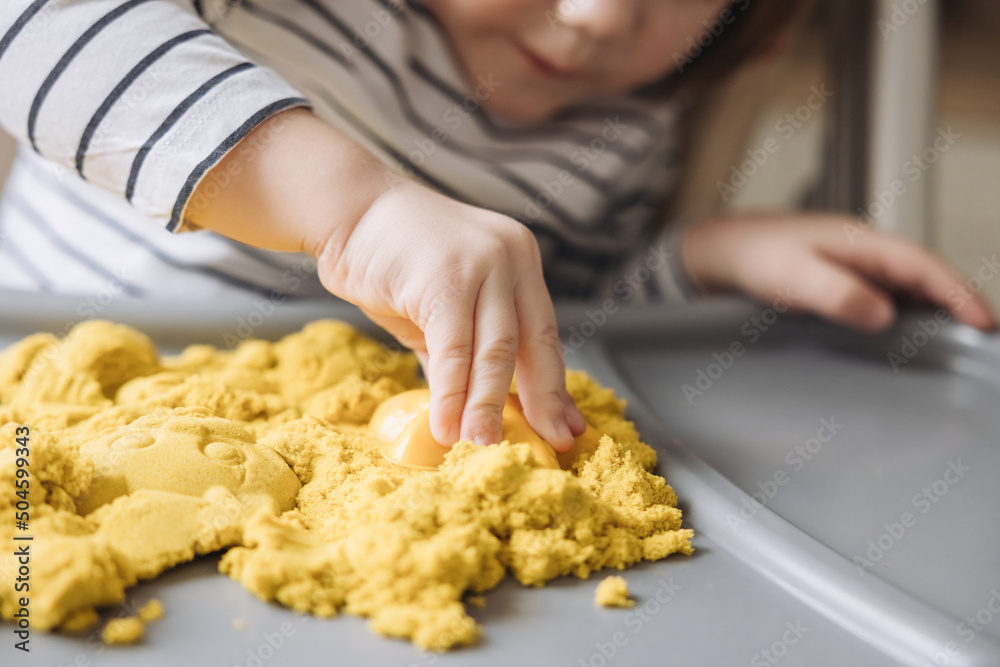 Hands of child moulding with magic kinetic sand. Cute little boy playing with kinetic sand. Development of fine motor skills. Early sensory education. Sand art therapy. Activities Montessori.
