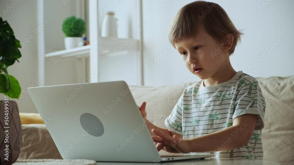 Child using laptop while sitting on sofa at home, Home schooling, distance learning Child using laptop while sitting on sofa at home, Home schooling, distance learning