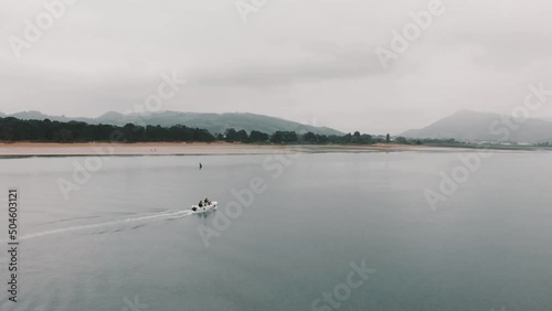 Small boat or yacht sailing alone on the estuary that leads to the sea on a cloudy day. At the bottom of the river the beach with vegetation and mountains. Drone shot air.