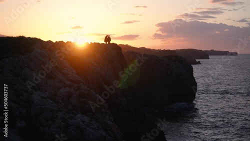 two silhouettes of people against the light in a reddish sunset on the cliffs by the sea that invites reflection and calm