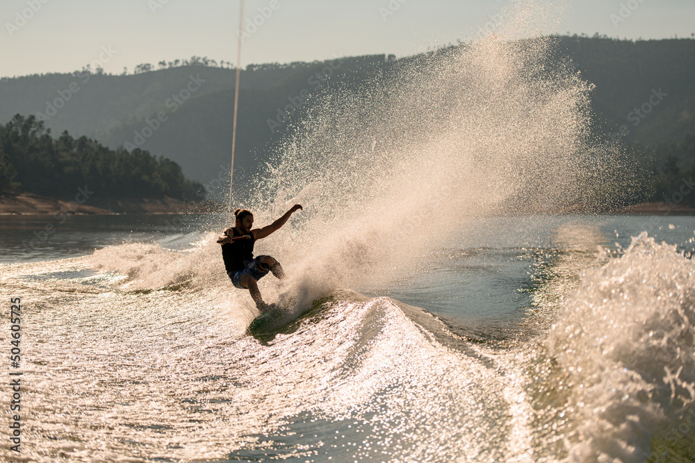 active man holds rope and energetically balancing on splashing wave on wakeboard