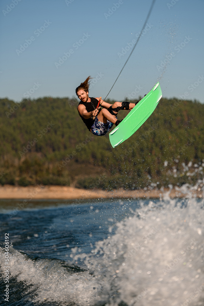 energy athletic guy holding a rope and jumping in the air with bright wakeboard