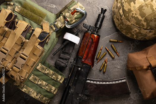 Military body armor, helmet and ammunition, a Kalashnikov assault rifle with matrons and a first aid tourniquet. On a black marble table. Army bulletproof vest. Flat lay. Military concept.