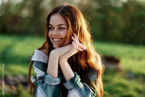 A beautiful woman outdoors in a green park laughs and smiles as she looks into the camera at sunset in the sun. Close-up portrait photo