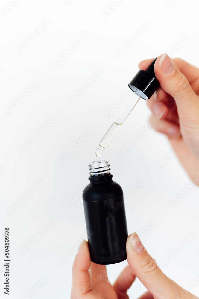 Woman's hands holding a pipette with natural oil on glass bottle Woman's hands holding a pipette with natural oil on glass bottle