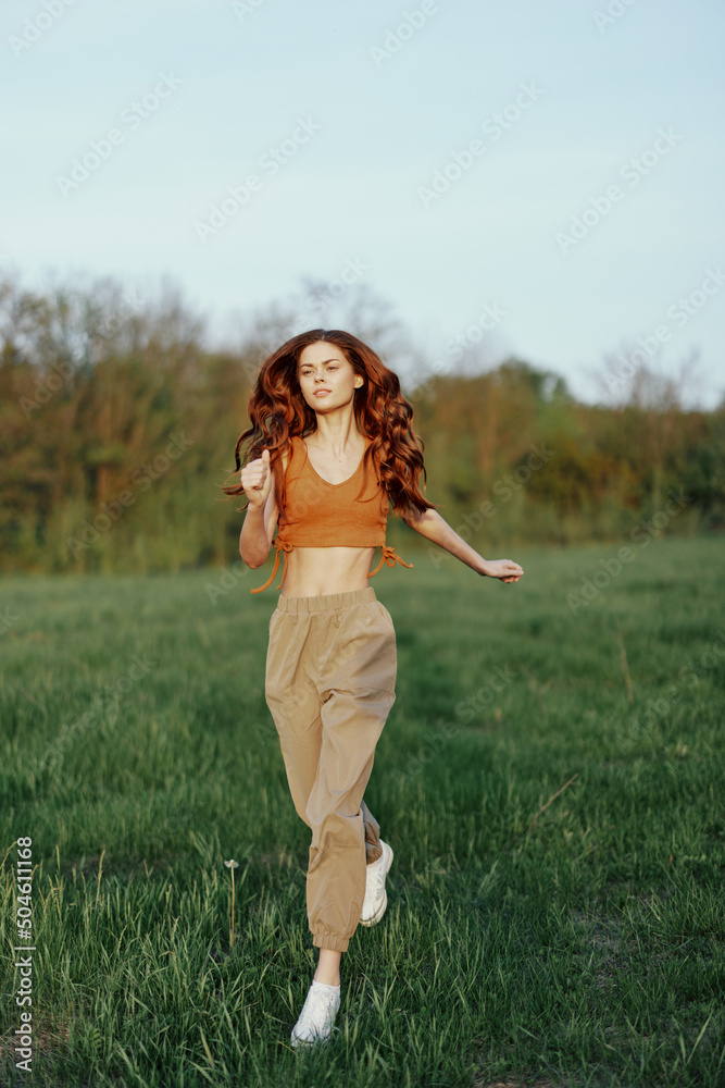 A woman of athletic build runs through the park on the green grass with loose, flying hair and working out into the sunset light