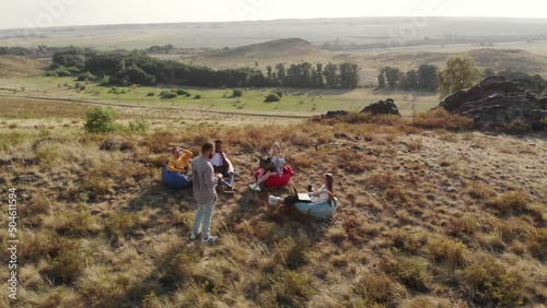 Group of freelancers are sitting in semicircle front of speaker on hill in chairs bag, with laptops on their knees, coffee mugs their hands, aerial view photo