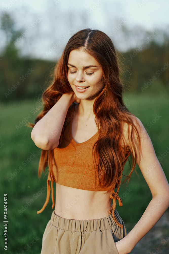 Naklejka premium Woman in nature with beautiful long curly hair enjoying the sunset sunshine and smiling while looking at the camera