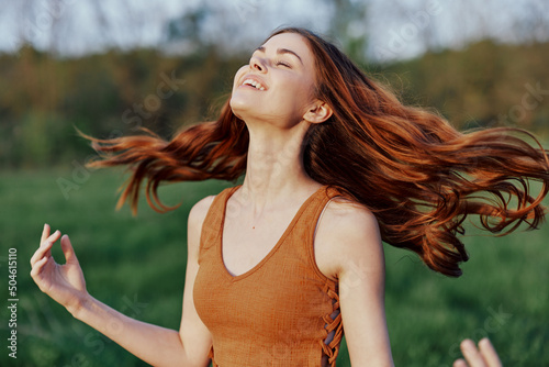 A young woman laughing and smiling merrily in nature in the park with the sunset lighting illuminating her long red hair