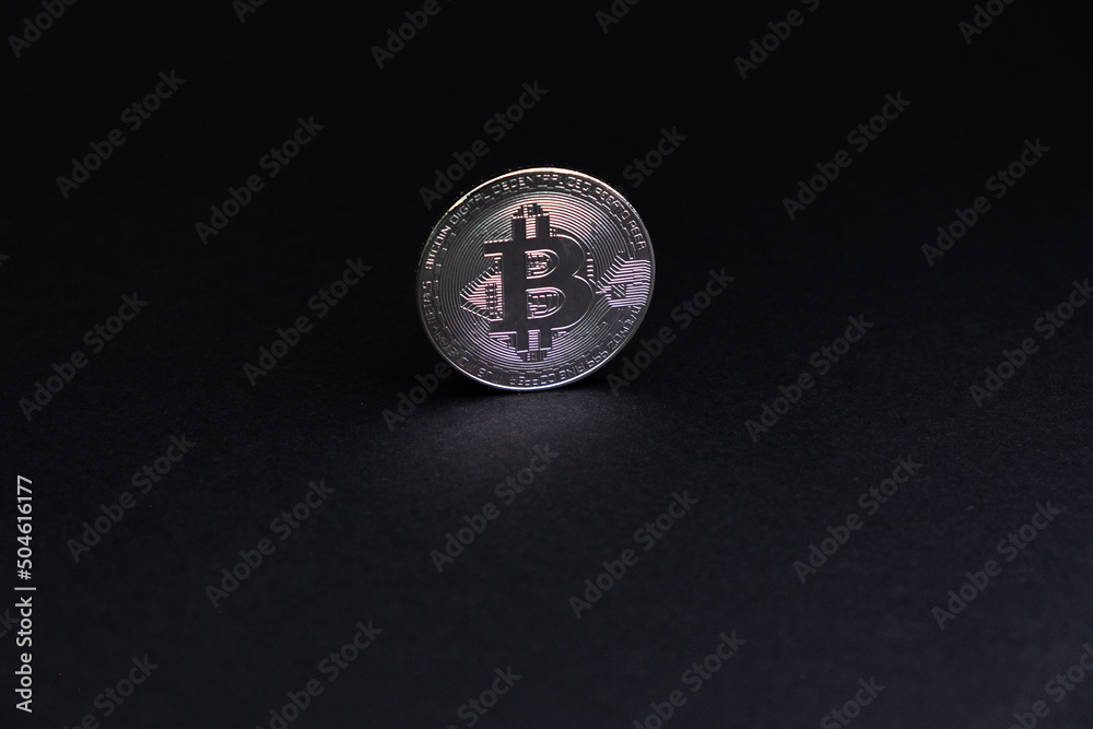 One BitCoin coin close-up with face on silver colour stand bottom centered on back background. Bitcoin BTC Digital crypto currency - Electronic Money. Digital coin international stock exchange. One BitCoin coin close-up with face on silver colour stand bottom centered on back background. Bitcoin BTC Digital crypto currency - Electronic Money. Digital coin international stock exchange.