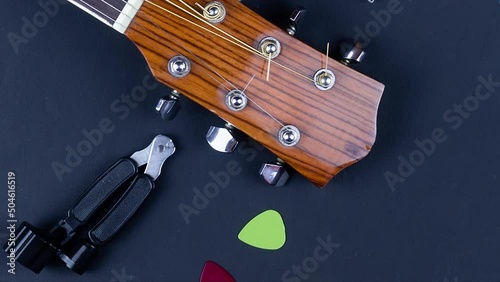 yellow guitar pick tucked into gold acoustic guitar strings on a dark wood fret board.