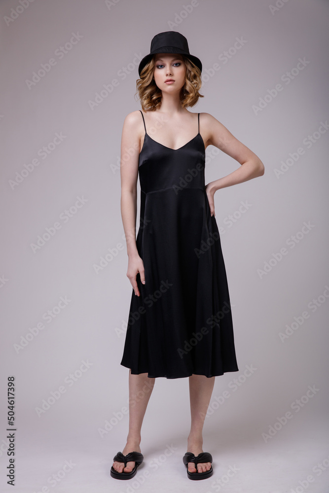 High fashion photo of a beautiful elegant young woman in a pretty black dress, hat posing over white, soft gray background. Hairstyle, slim figure. Studio Shot. High fashion photo of a beautiful elegant young woman in a pretty black dress, hat posing over white, soft gray background. Hairstyle, slim figure. Studio Shot.