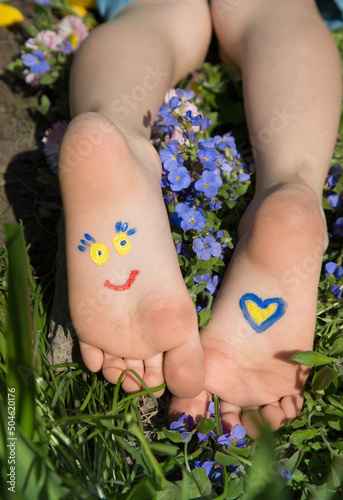 smiling face, heart are painted on children's bare feet in yellow and blue colors of Ukrainian flag. Children against war. Hello summer. attracting attention of world community to war in Ukraine photo