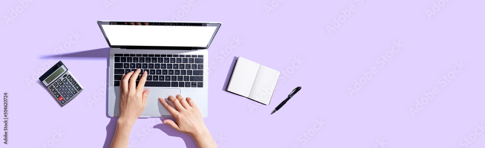 Person using a laptop computer with a notebook and a calculator - obrazy, fototapety, plakaty 