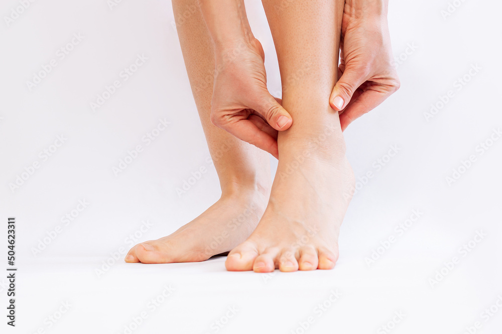 Cropped shot of a young woman touching painful twisted or broken ankle with her hands isolated on a white background. The girl twisted her leg. Sport injury, painful sprained ankle muscle Cropped shot of a young woman touching painful twisted or broken ankle with her hands isolated on a white background. The girl twisted her leg. Sport injury, painful sprained ankle muscle