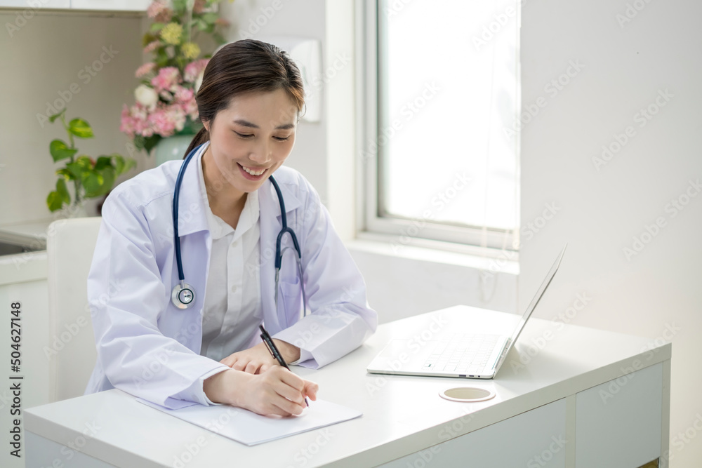 Young Female Doctor in white coat sitting at her workplace working. Doctor sitting at desk and writing a prescription for her patient. Smiling female doctor working in doctor’s office. Young Female Doctor in white coat sitting at her workplace working. Doctor sitting at desk and writing a prescription for her patient. Smiling female doctor working in doctor’s office.