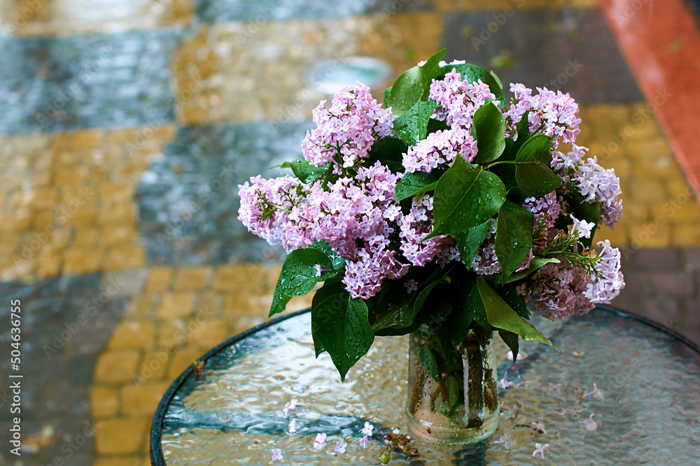 Lilac branches in a glass vase in the rain in the old city