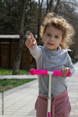 Child on a scooter in the park. A little girl rides a scooter on a sunny day. Active sports for preschoolers